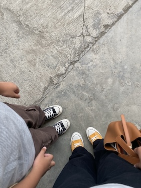 mom and child standing on the sidewalk together with only their feet and legs showing